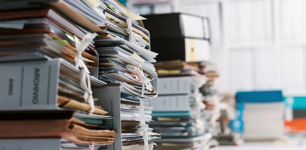 Piles de dossiers papier accumulés dans un bureau